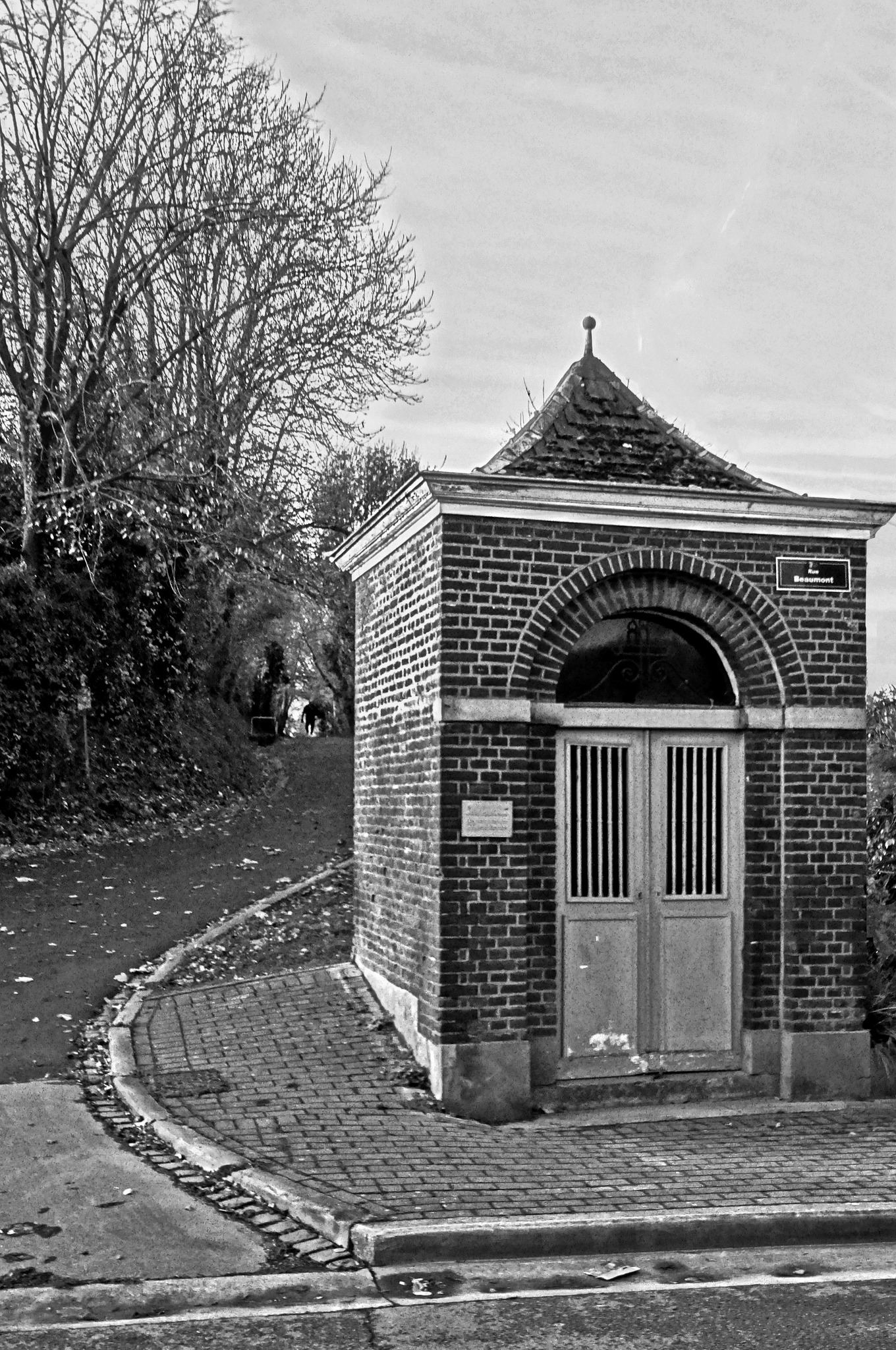 La chapelle de Beaumont aujourd'hui, au coin de la rue : murs de briques, toit d'ardoises en pointe couvert de mousse, porte à deux battants.