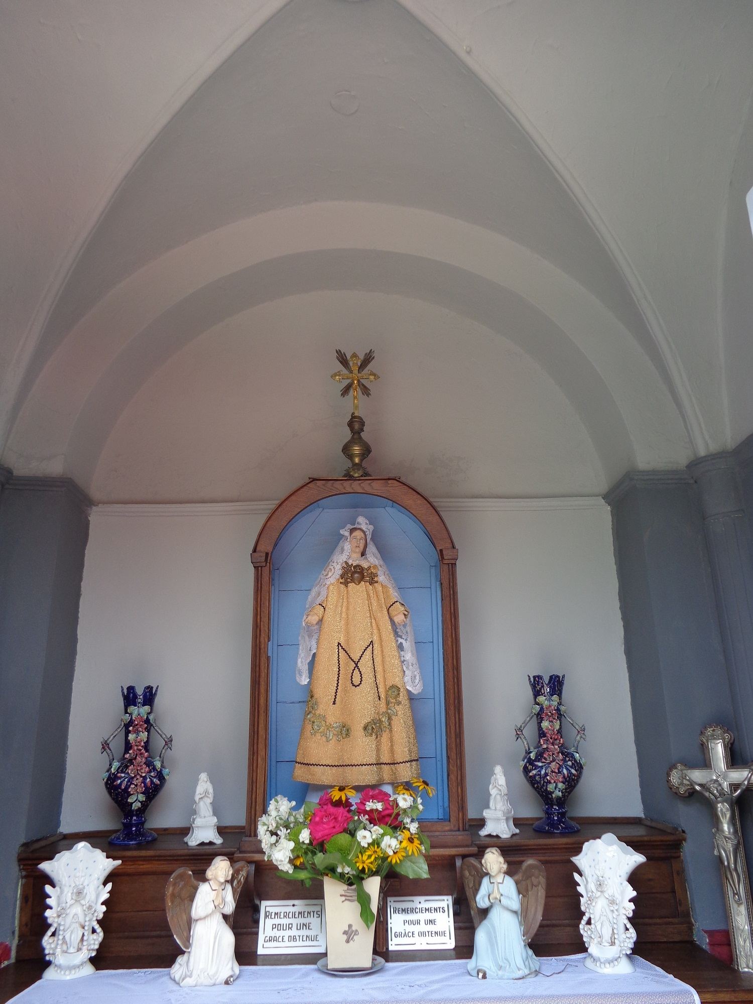 L'autel : la statue habillée de Notre-Dame des Sept Douleurs dans sa niche bleue, entre des vases, des anges et des plaques de remerciement.